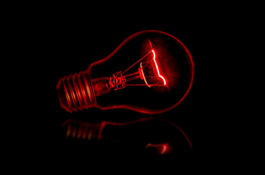 Eine Glühbirne unter rotem Licht vor schwarzem Hintergrund.