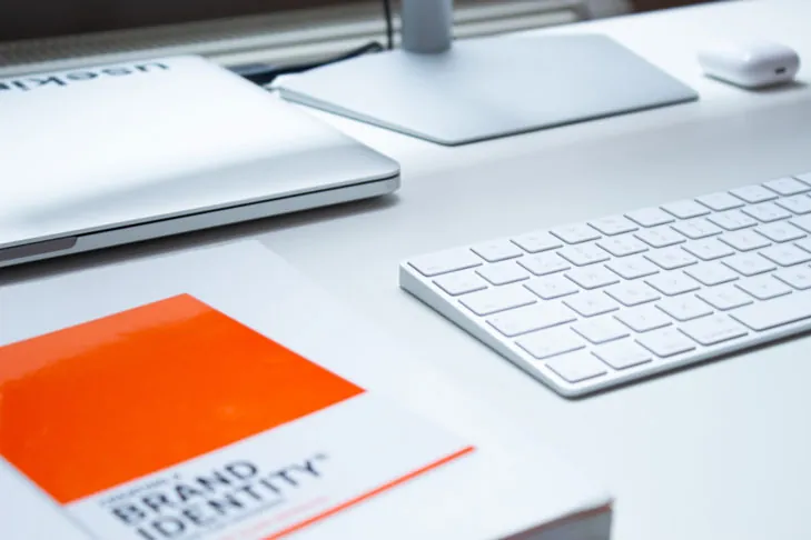 Eine Tastatur, ein Notebook und ein Buch über Brand Identity liegen auf einem Tisch.